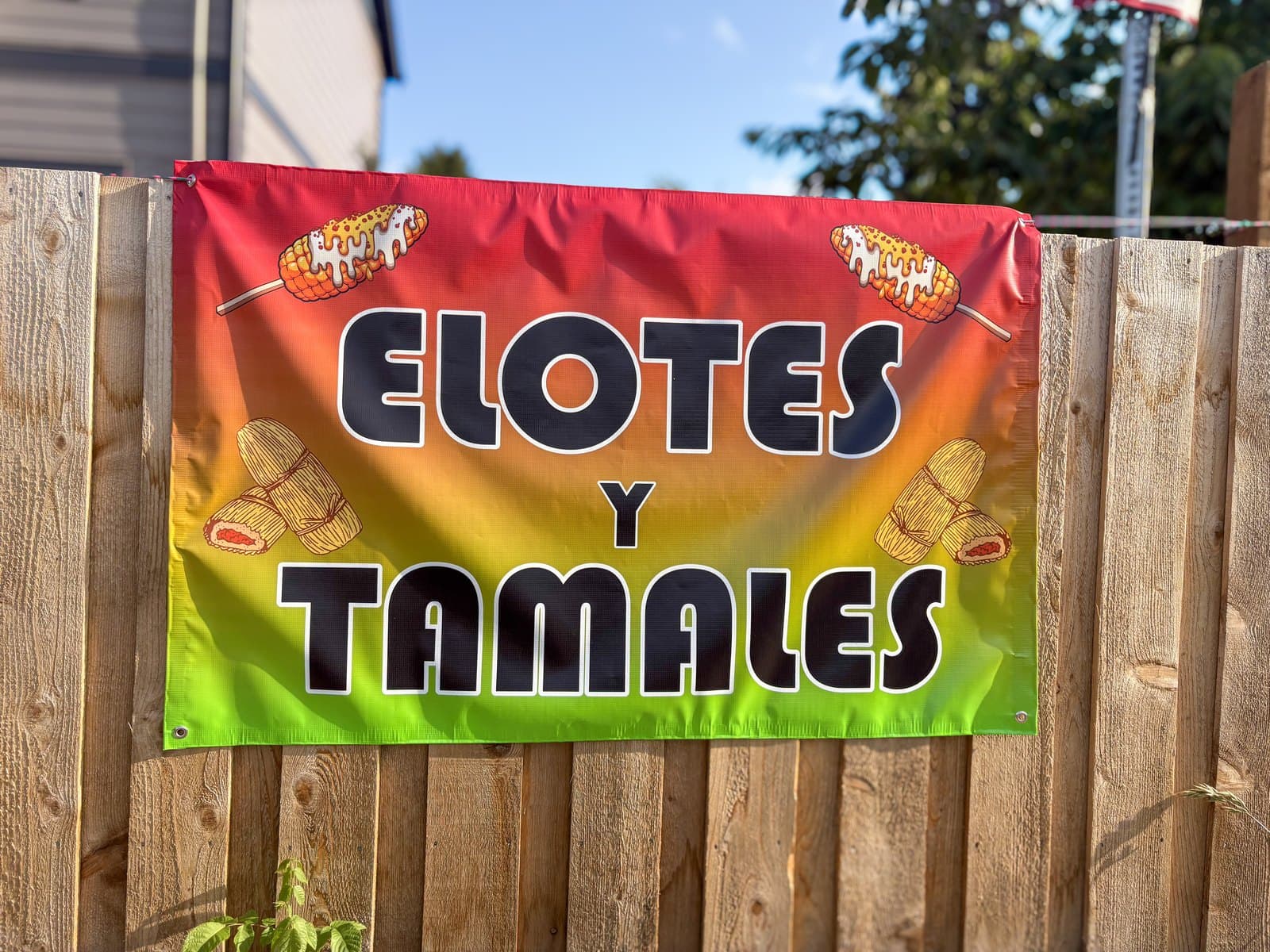 A printed vinyl banner for a food stand, hung on a wooden fence