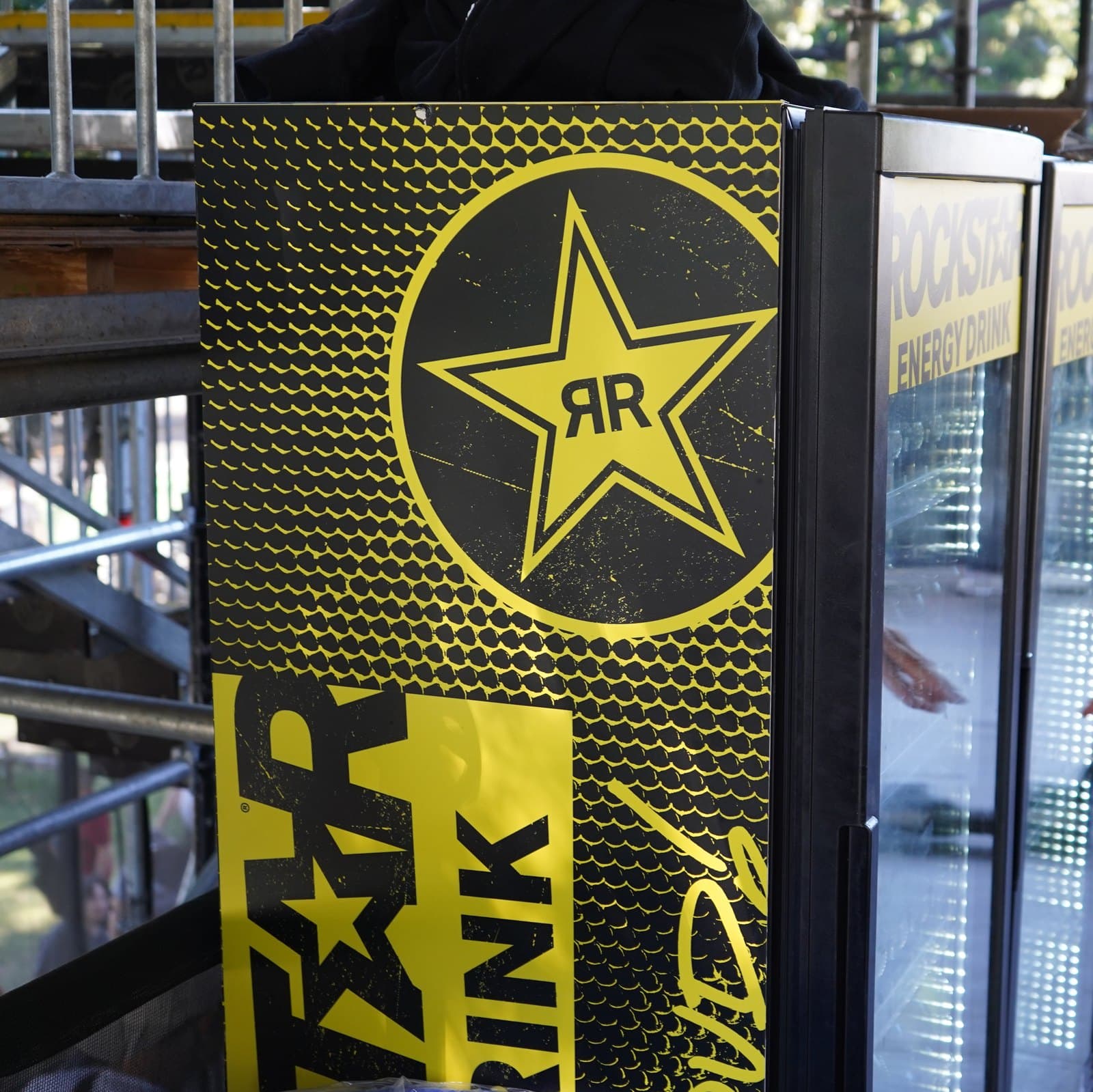 A drinks fridge wrapped in a black and yellow printed graphic at an outdoor event
