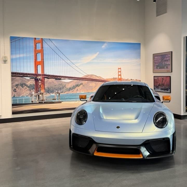 A printed mural of a suspension bridge covering a showroom wall, with a sports car parked in front of it