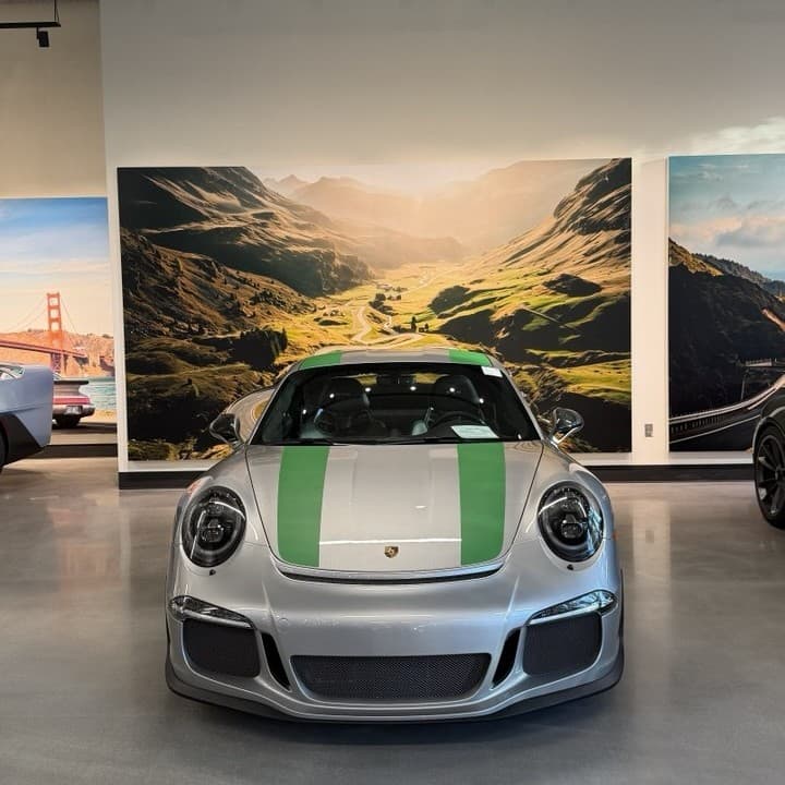 A printed mural of a green valley covering a showroom wall, with a sports car parked in front of it