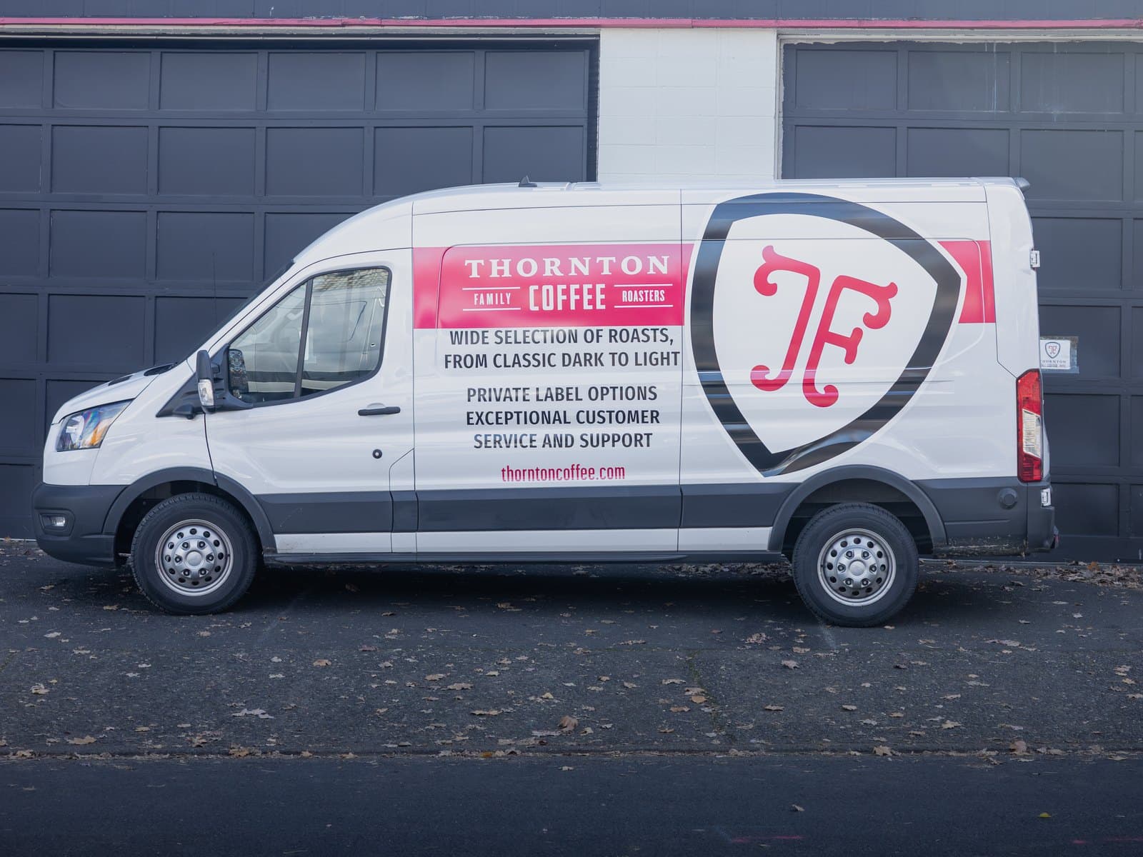 A white cargo van with printed graphics along its side, parked in front of a dark building